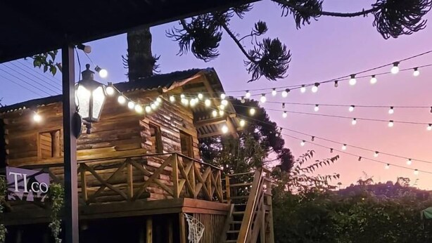 A rustic wooden cabin with a balcony, string lights, and a sign reading 'TI.CO'. - Tico Pousada - Campos do Jordão (Campos do Jordão)