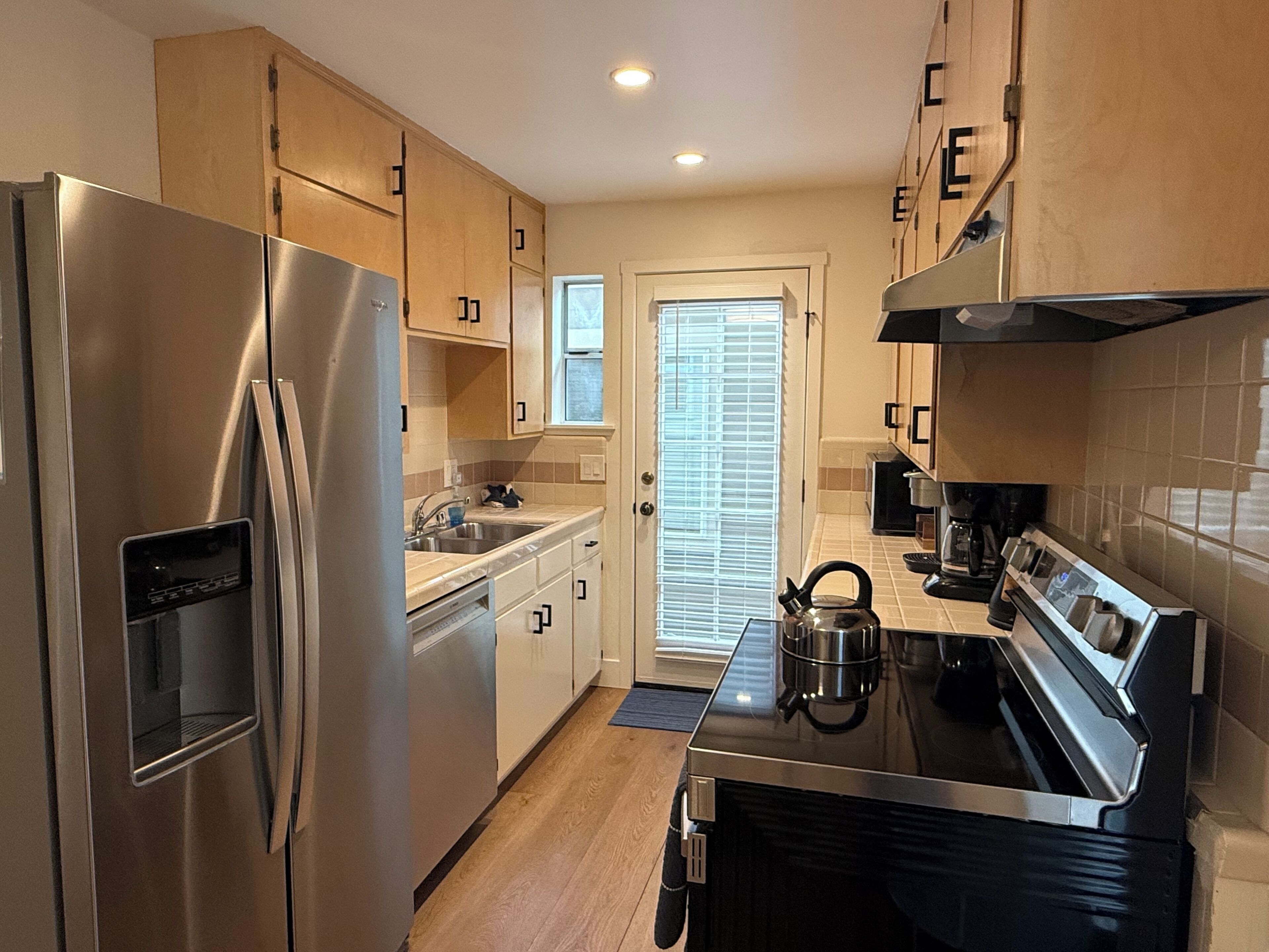 Una cocina moderna con electrodomésticos de acero inoxidable, armarios de madera y una ventana con persianas.