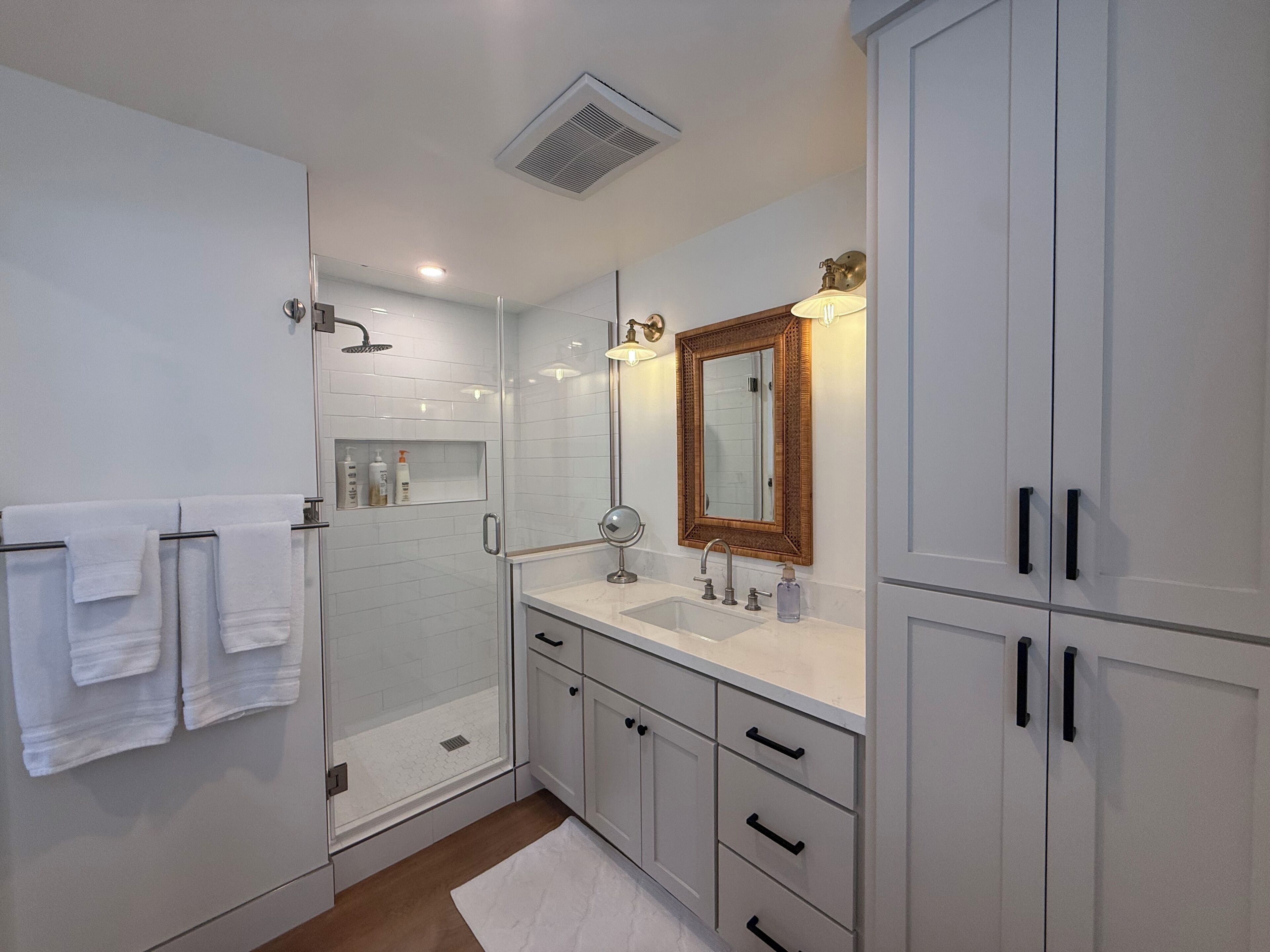 A modern bathroom with a glass shower enclosure, white cabinetry, and a large mirror.