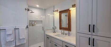 A modern bathroom with a glass shower enclosure, white cabinetry, and a large mirror.