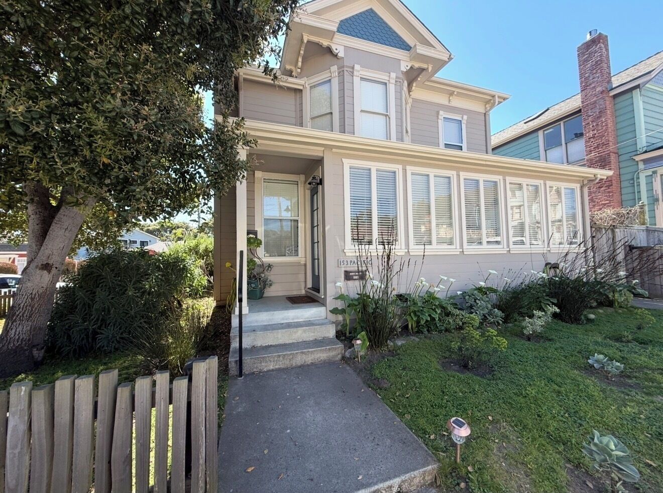 A two-story house with a front porch, a small garden, and a wooden fence.