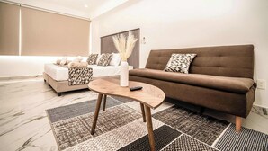 En moderne stue med sofa, sofabord og seng med mønstrede puder.
