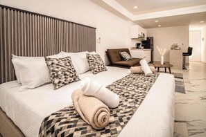 Ein modernes Hotelzimmer mit einem großen Bett, einer Couch, einem kleinen Tisch und einer Küchenzeile.