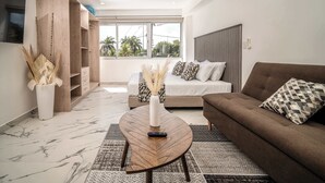 Uma sala de estar moderna com sofá, mesa de centro, televisão e uma janela grande com vista para palmeiras.