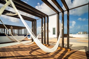 Un hamac sur une terrasse en bois, avec vue sur les bâtiments et le ciel.