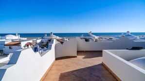 Une terrasse sur le toit, avec des bâtiments blancs, un ciel bleu dégagé et une vue sur la mer.