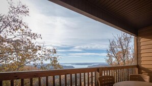 A wooden deck with a table and chairs, overlooking a scenic view of trees and a body of water. - The Lodges at Table Rock Lake (Branson)