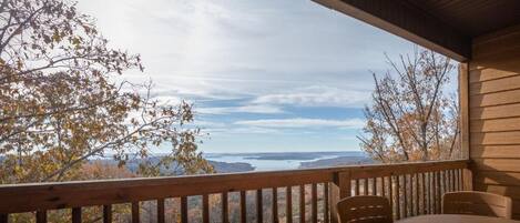 A wooden deck with a table and chairs, overlooking a scenic view of trees and a body of water.
