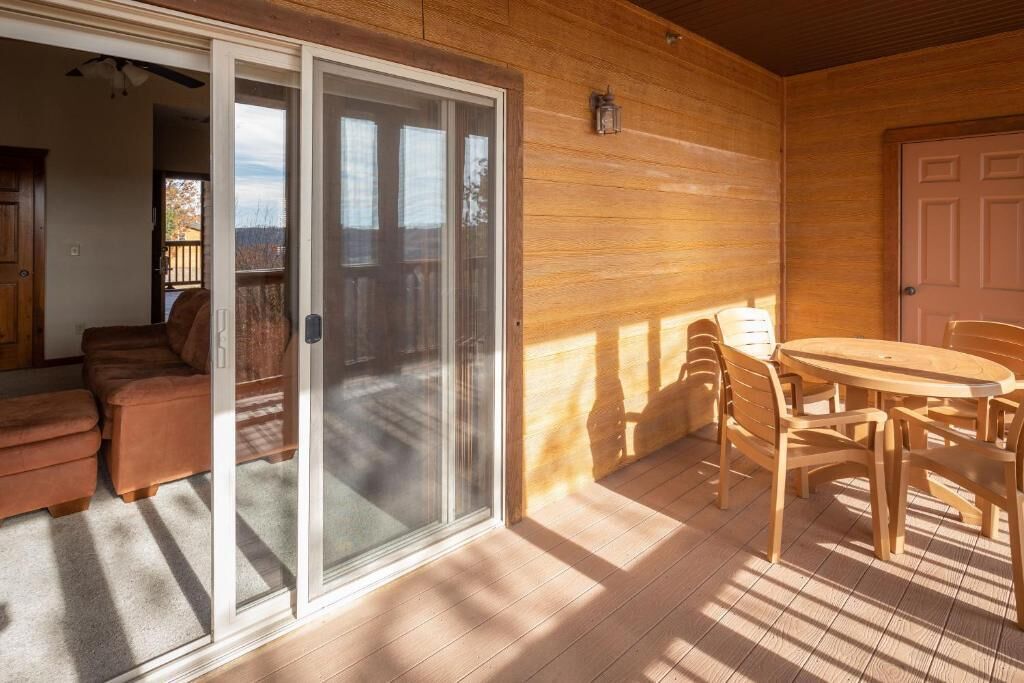 A wooden deck with a sliding glass door leading to a balcony, a round wooden table with chairs, and a door to the right.
