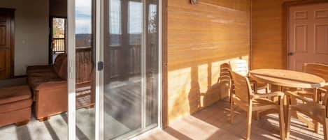 A wooden deck with a sliding glass door leading to a balcony, a round wooden table with chairs, and a door to the right.