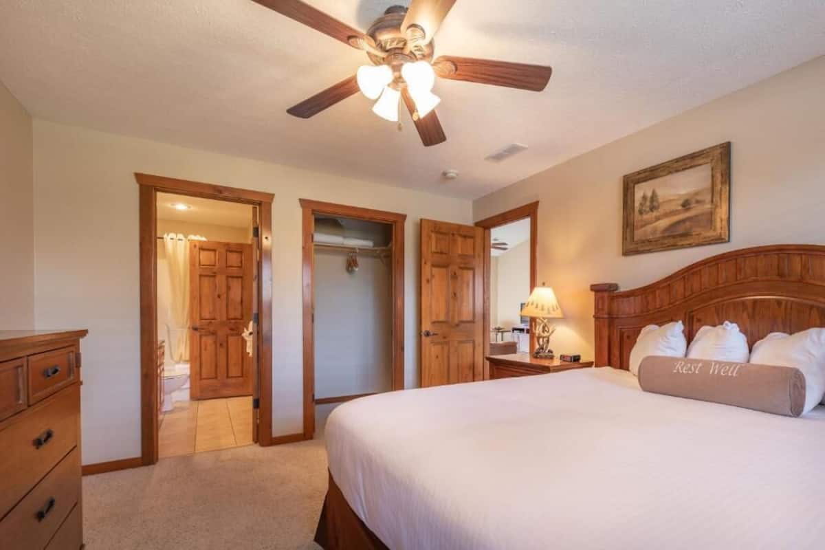 A bedroom with a bed, a ceiling fan, a nightstand, a lamp, and a painting on the wall.