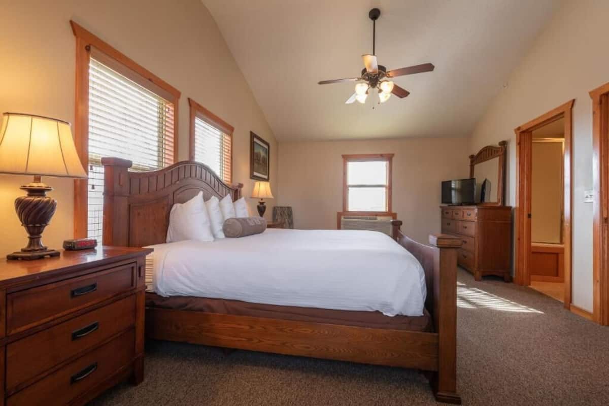 A bedroom with a wooden bed, a nightstand, a dresser, a ceiling fan, and a window with blinds.