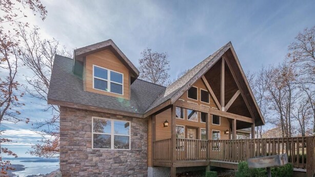 A two-story log cabin with a stone exterior, a wooden deck, and a view of a lake. - The Lodges at Table Rock Lake (Branson)