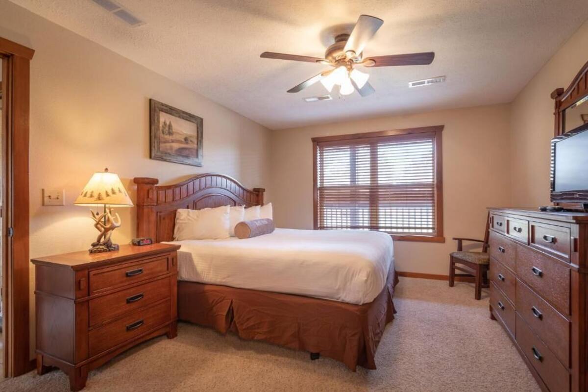 A bedroom with a bed, a nightstand, a dresser, a ceiling fan, and a window with blinds.