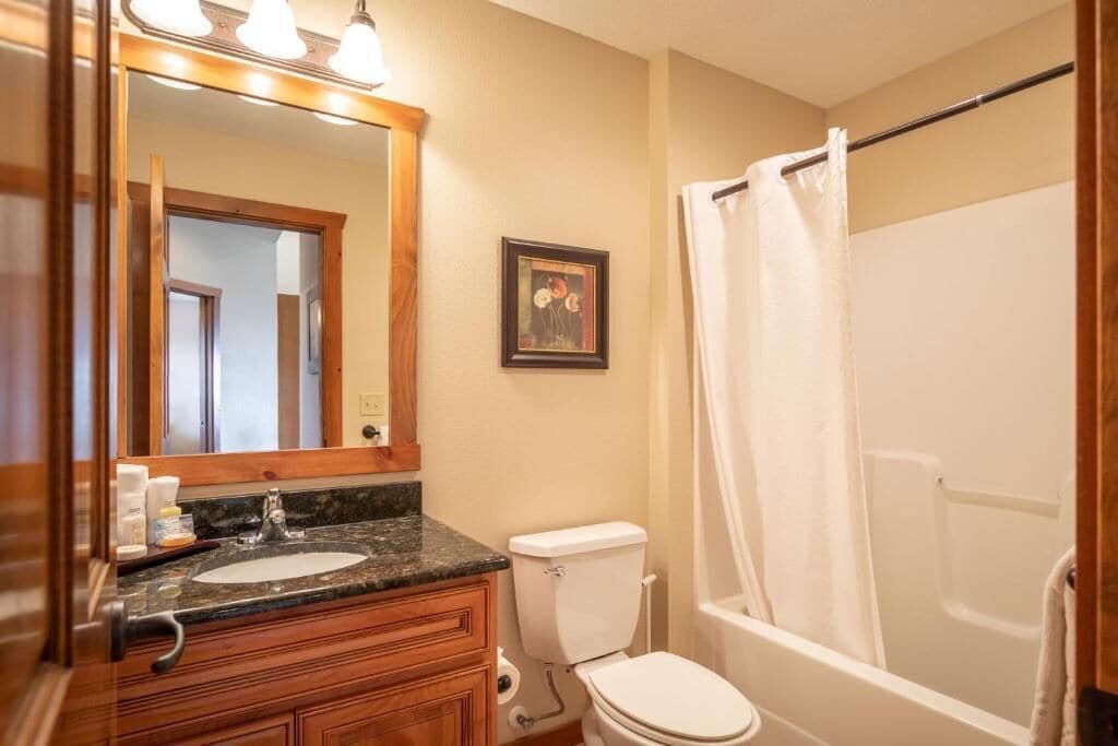 A bathroom with a wooden vanity, a sink, a toilet, and a bathtub with a shower curtain.