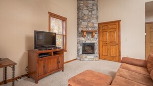 A living room with a stone fireplace, a television on a wooden stand, and a brown sofa. - The Lodges at Table Rock Lake (Branson)