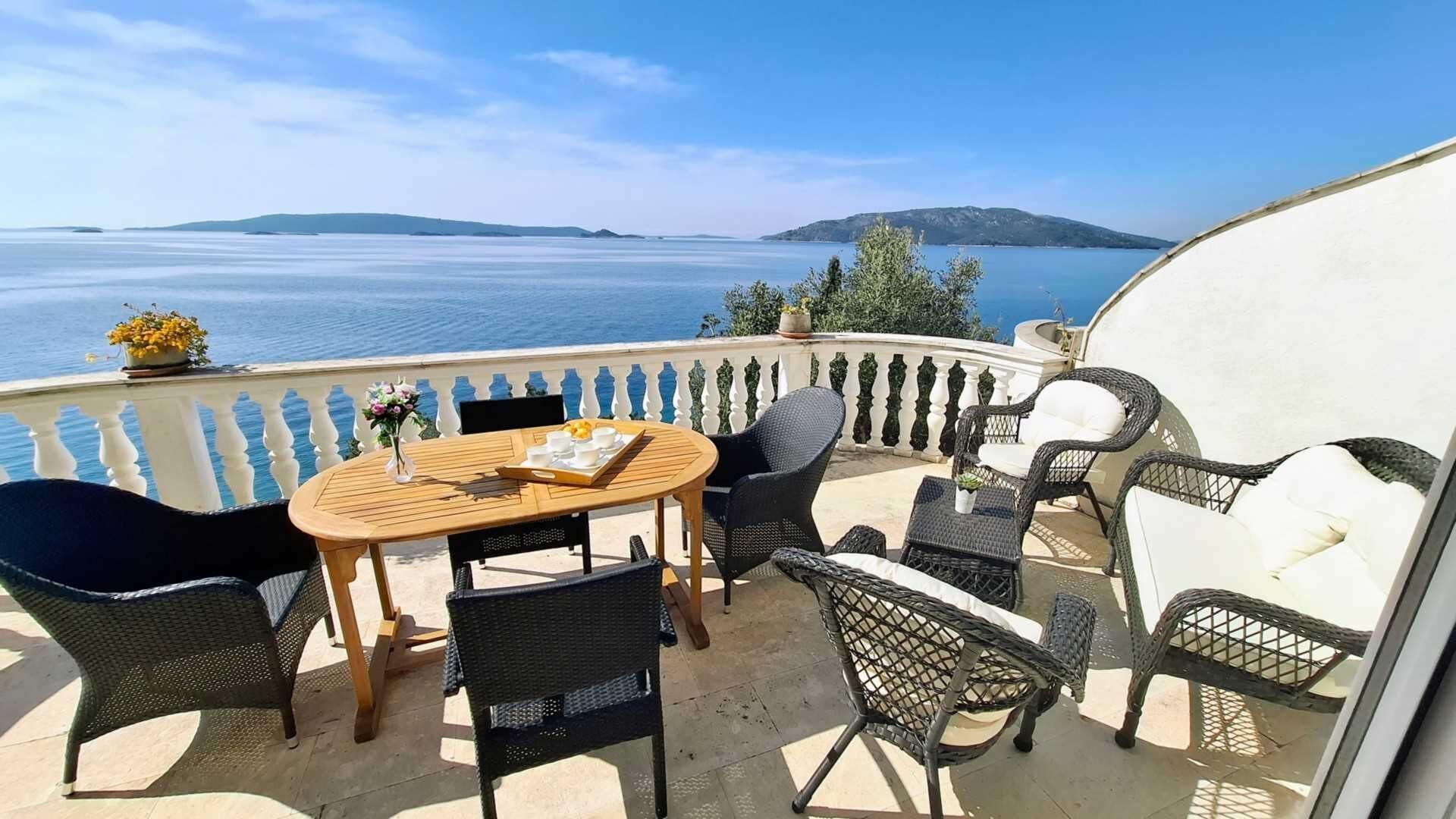 A balcony with a wooden table and chairs, overlooking a body of water and distant land.