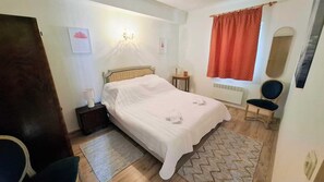 A bedroom with a bed, bedside table, lamp, chair, window with red curtains, and a radiator. - Beachside apartment Belle Vue 1 (Okrug Donji)