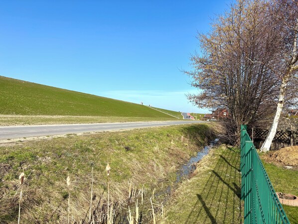 A rural road with a green fence, a small stream, and a hill in the background.