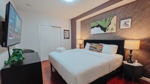 A neatly arranged hotel room with a bed, bedside lamps, a TV, and a door. - Helix / King Bed / Elevator  Adjustable Desk (Philadelphia)