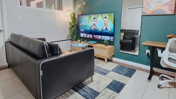 A living room with a sofa, a TV, a coffee table, and a small desk with a chair. - Helix / King Bed / Elevator  Adjustable Desk (Philadelphia)