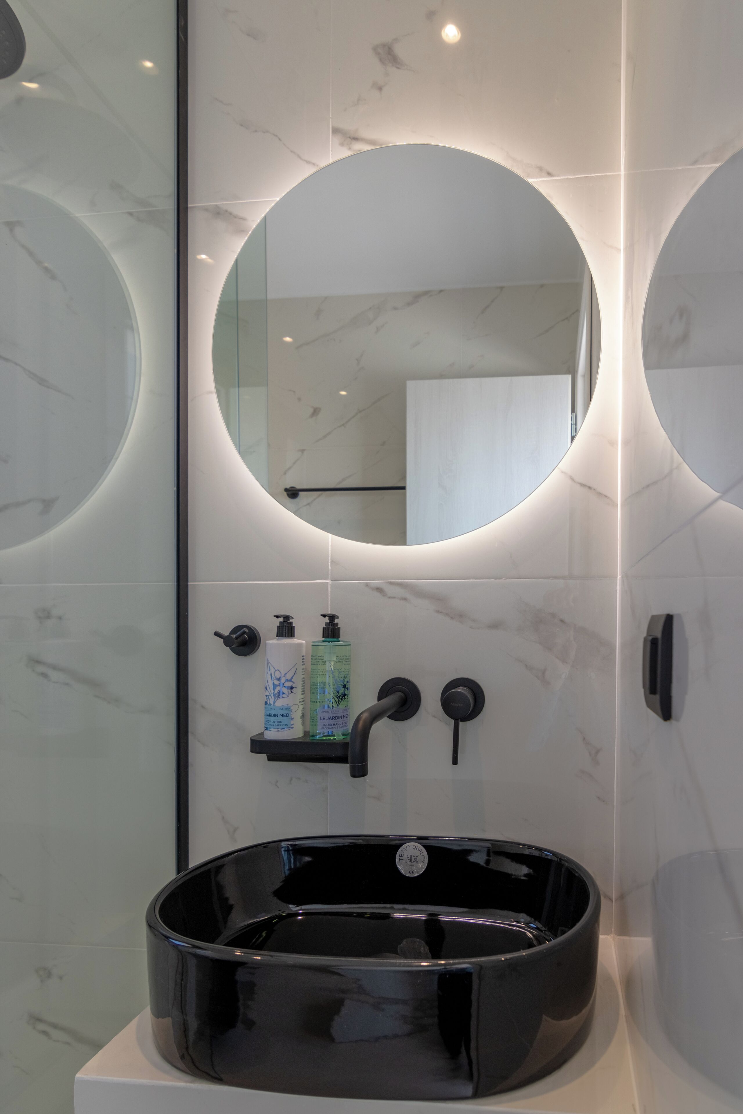 Een moderne badkamer met een ronde spiegel, een zwarte wastafel en een douchecabine van glas.