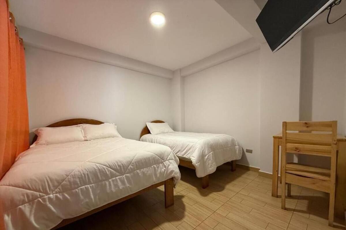 A room with two beds, a wooden chair, and a TV mounted on the wall.