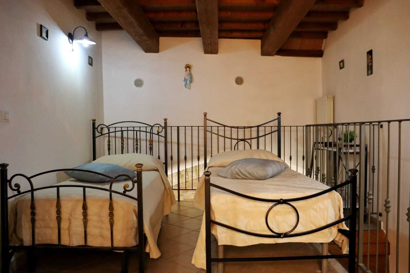 Una habitación con dos camas de estructura metálica, techo de madera y una pequeña lámpara fijada a la pared.