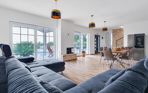 Ein modernes Wohnzimmer mit einer großen Eckcouch, einem Essbereich mit einem Holztisch und Stühlen sowie einer Küche mit Kühlschrank und Fernseher.