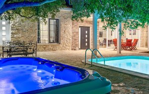 Ein Whirlpool und ein Schwimmbecken mit Steinmauern, Gartenmöbeln und einer überdachten Terrasse.