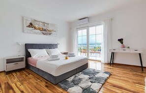 Ein modernes Schlafzimmer mit Bett, Nachttischen, einem Schreibtisch und Blick auf einen Balkon.