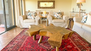 A living room with two white armchairs, a wooden coffee table, a red patterned rug, and a large mirror on the wall.