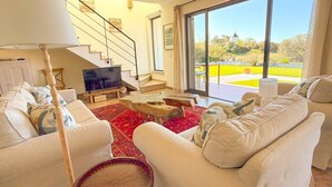 A spacious living room with a large TV, comfortable seating, a staircase, and a view of the outdoors.