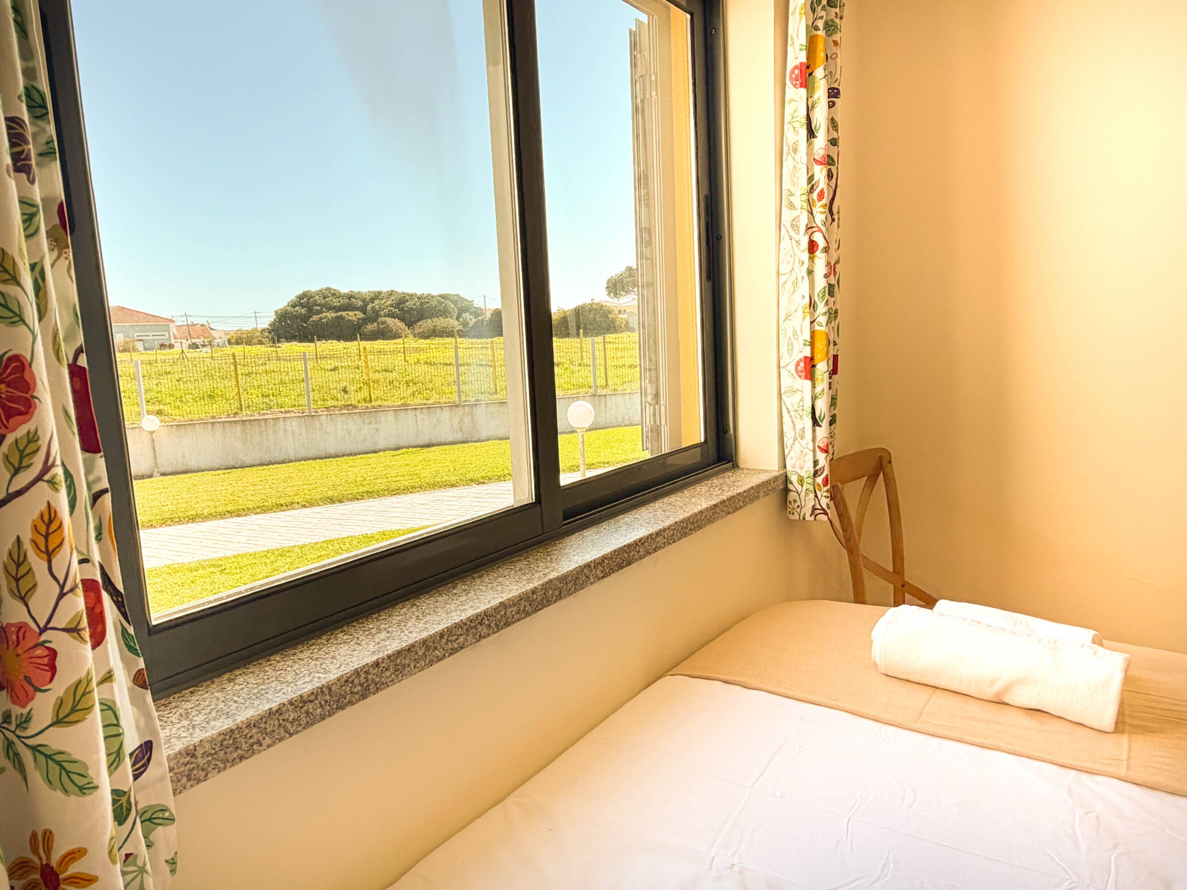 Un dormitorio con cama, una ventana con cortinas y vistas a un campo verde.