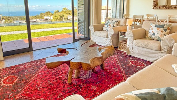 A living room with a large glass door leading to a balcony, a red patterned rug, and a wooden sculpture.