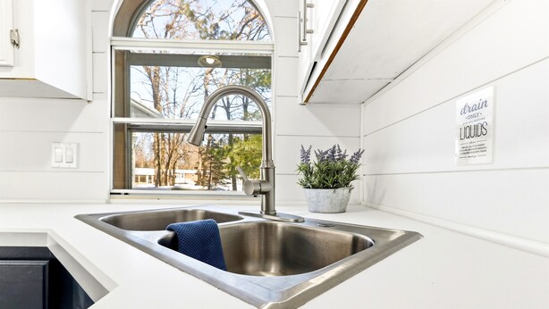 A kitchen with a stainless steel sink, a window, and a potted plant. - Feather Trail Guest House - 3BR Cozy Family Stay (Nekoosa)