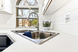 A kitchen with a stainless steel sink, a window, and a potted plant. - Feather Trail Guest House - 3BR Cozy Family Stay (Nekoosa)