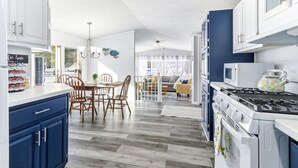 A modern kitchen with white cabinets, a dining area with wooden chairs, and a view through a glass door to a living room. - Feather Trail Guest House - 3BR Cozy Family Stay (Nekoosa)