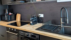 A modern kitchen with a built-in washer, a microwave, and a sink with a wooden cutting board. - Zen Sakura - The Breath of Asia! (Belfort)