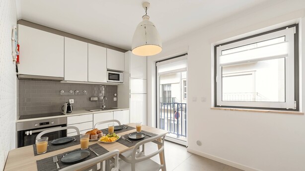 Una cocina moderna con armarios blancos, un microondas y una mesa de comedor con platos, vasos y frutero.