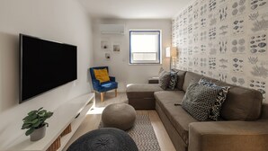 Una sala moderna con un televisor de pantalla plana, un sillón azul, un sofá marrón y una pared decorada con ilustraciones marinas.