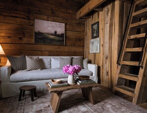 A wooden interior with a sofa, a coffee table with books, and a painting on the wall. - Asheville Ivy Cabin - Superhost (Black Mountain)