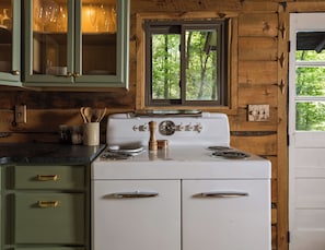A kitchen with a stove, cabinets, and a window with a view of trees. - Asheville Ivy Cabin - Superhost (Black Mountain)