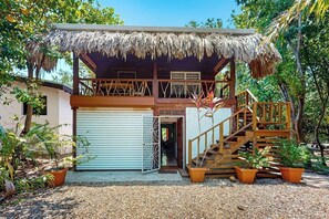 A two-story building with a thatched roof, a covered balcony, and a staircase leading to the upper level. - Charming duplex with full Kitchen & WiFi - near dining & stunning attractions (Placencia)