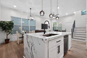 A modern kitchen with a marble countertop, a built-in dishwasher, and pendant lighting. - East End Stay | Near Daikin Park & Downtown (Houston)