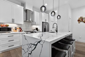 A modern kitchen with white cabinetry, a marble island, stainless steel appliances, and pendant lighting. - East End Stay | Near Daikin Park & Downtown (Houston)