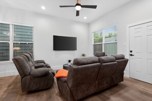 Ein modernes Wohnzimmer mit einem an der Wand befestigten Flachbildfernseher, einem Deckenventilator und einer Sitzecke mit zwei Fernsitzmöbeln.