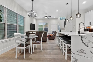 Una cocina moderna con encimera de mármol, armarios blancos y una zona de comedor con sillas y mesa blancos.