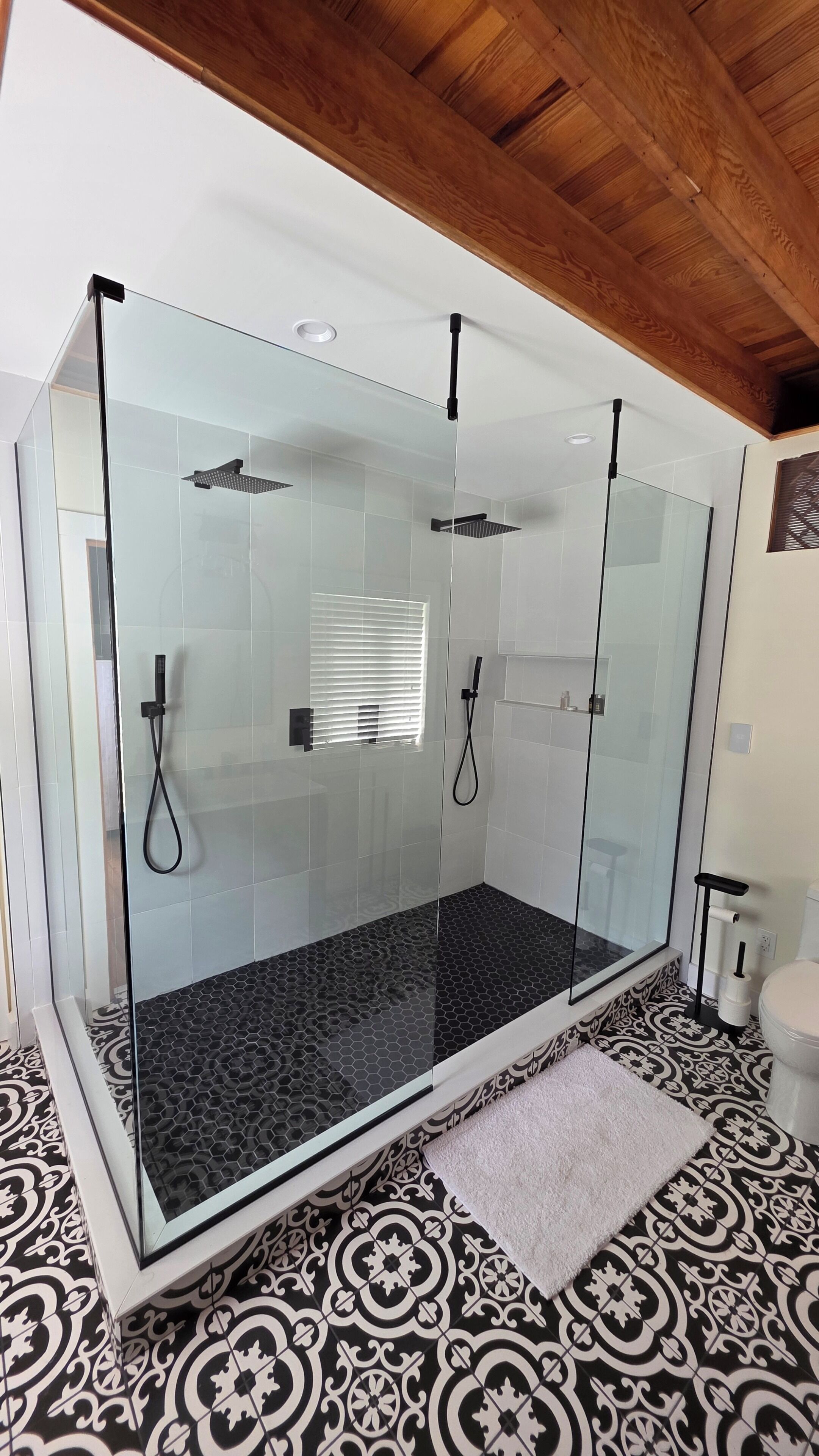 A glass-enclosed shower with a black patterned floor, a white towel, and a wooden ceiling.