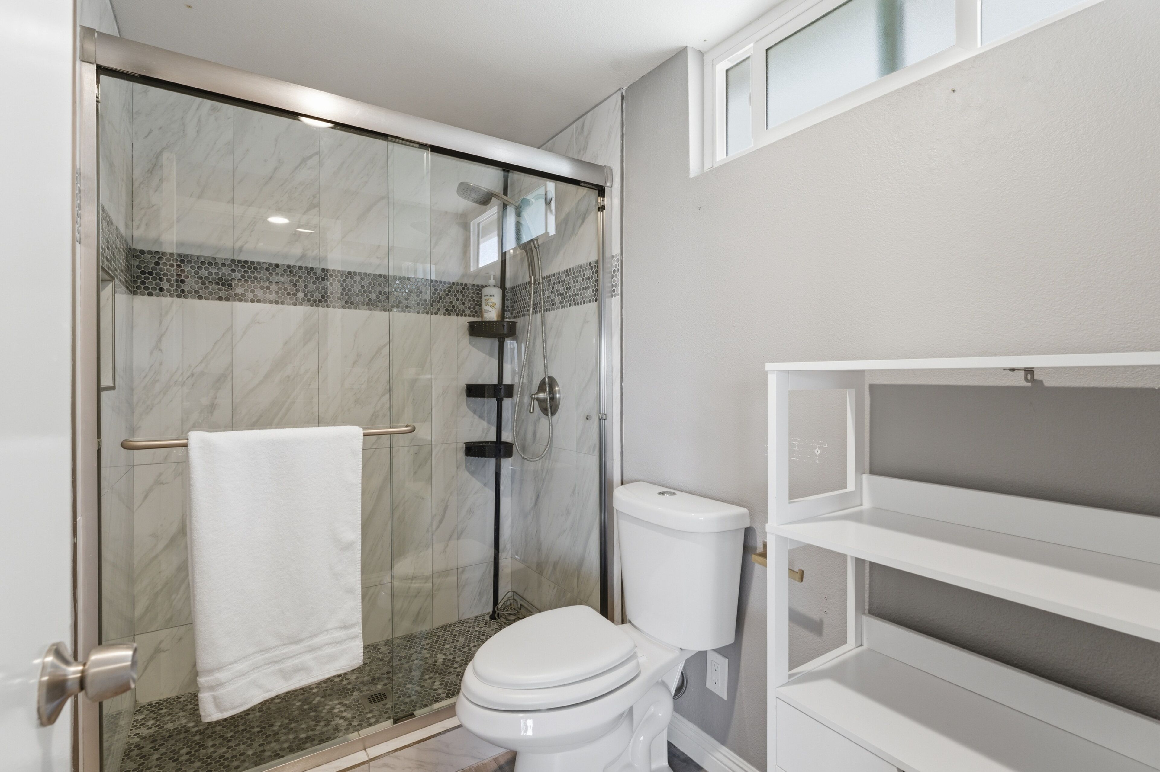 A bathroom with a glass-enclosed shower, a toilet, and a white towel rack.